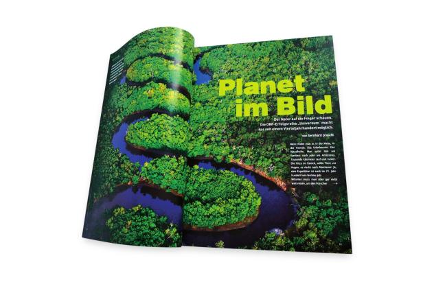 … Eine Doppelseite einer Zeitschrift zeigt eine Luftaufnahme eines Flusses, der sich durch dichten grünen Dschungel schlängelt.