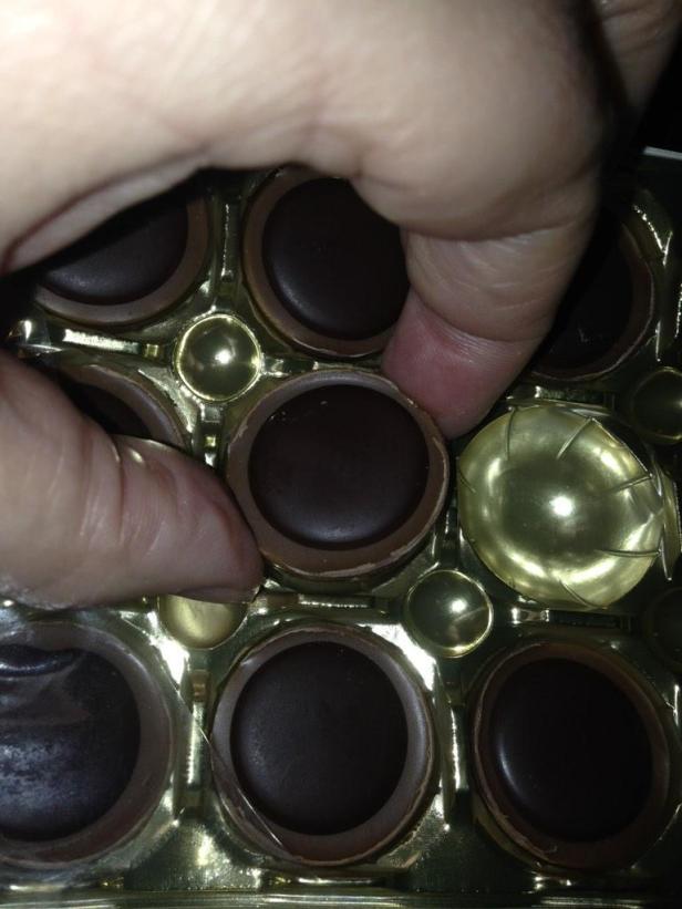 Eine Hand nimmt eine Praline aus einer goldenen Schachtel.