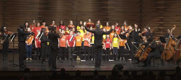 Ein Kinderchor und ein Orchester treten auf einer Bühne auf.