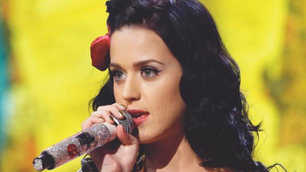 Katy Perry singt mit einem mit Strasssteinen besetzten Mikrofon vor einem gelben Hintergrund.