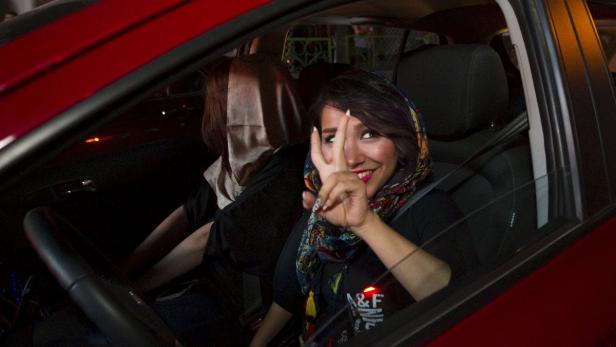 Eine Frau mit Kopftuch sitzt in einem roten Auto und zeigt ein Victory-Zeichen.