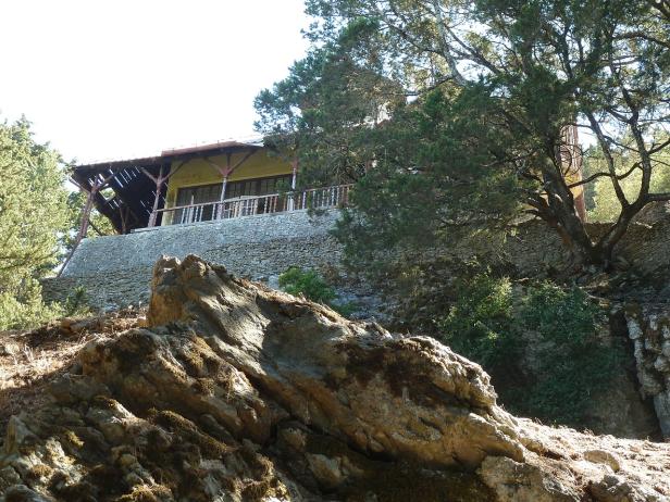 Ein Haus mit Balkon steht auf einer steinernen Anhöhe, umgeben von Bäumen.