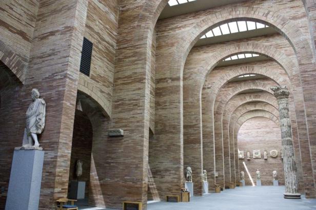 Ein langer Saal mit Ziegelwänden, Bögen und Statuen an den Seiten.