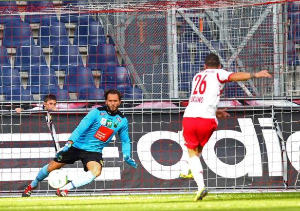 Ein Fußballspieler schießt einen Elfmeter, während der Torwart versucht, den Ball abzuwehren.