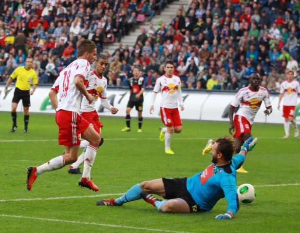 Ein Fußballspiel mit Spielern in roten und weißen Trikots und einem Torwart in blauem Trikot.