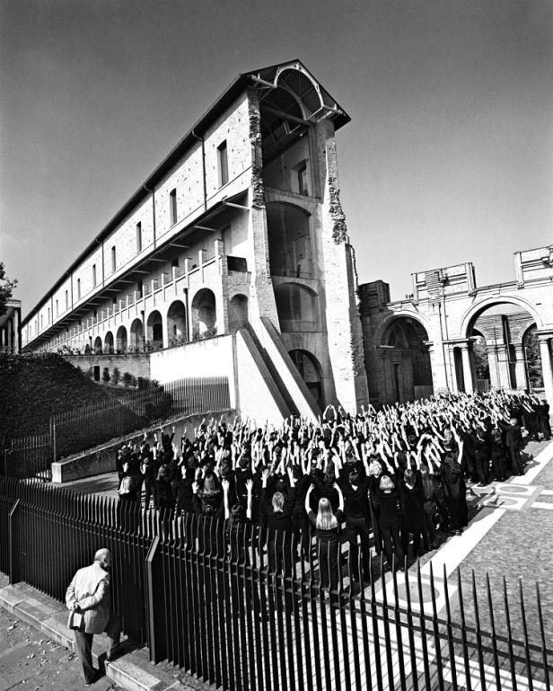 Eine große Gruppe von Menschen steht vor einem Gebäude und reckt die Arme in die Höhe.