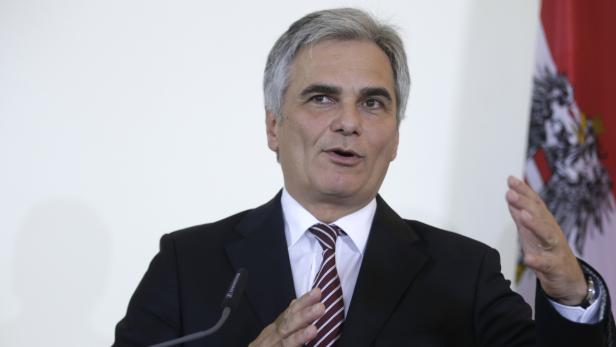 Ein Mann in einem Anzug gestikuliert vor einer österreichischen Flagge.