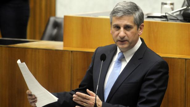 Ein Mann im Anzug hält ein Blatt Papier in der Hand und spricht an einem Rednerpult.