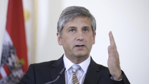 Ein Mann in einem Anzug spricht vor einer österreichischen Flagge.