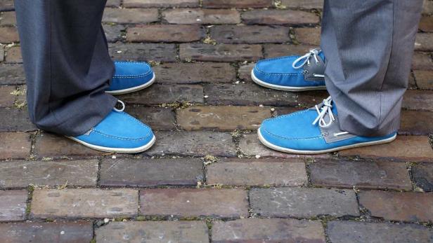 Zwei Personen stehen sich gegenüber und tragen blaue Schuhe auf einem Backsteinpflaster.