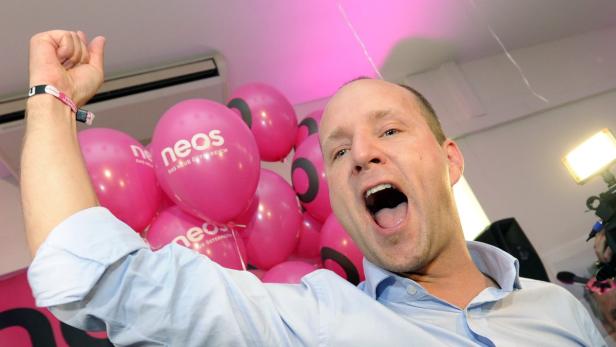 Ein Mann jubelt mit erhobener Faust vor pinkfarbenen NEOS-Luftballons.