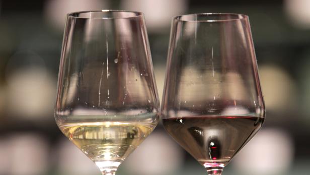 Zwei Weingläser, eines mit Weißwein und eines mit Rotwein, stehen nebeneinander.