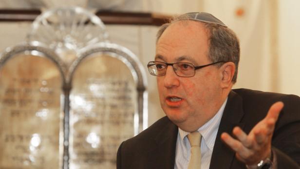 Ein Mann mit Kippa gestikuliert vor einer Tafel mit hebräischen Schriftzeichen.