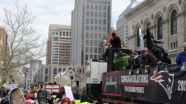 Eine Parade der New England Patriots in Boston vor einer Menschenmenge und hohen Gebäuden.