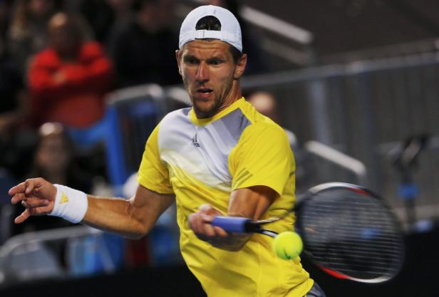 Ein Tennisspieler in gelbem Hemd schlägt einen Ball.