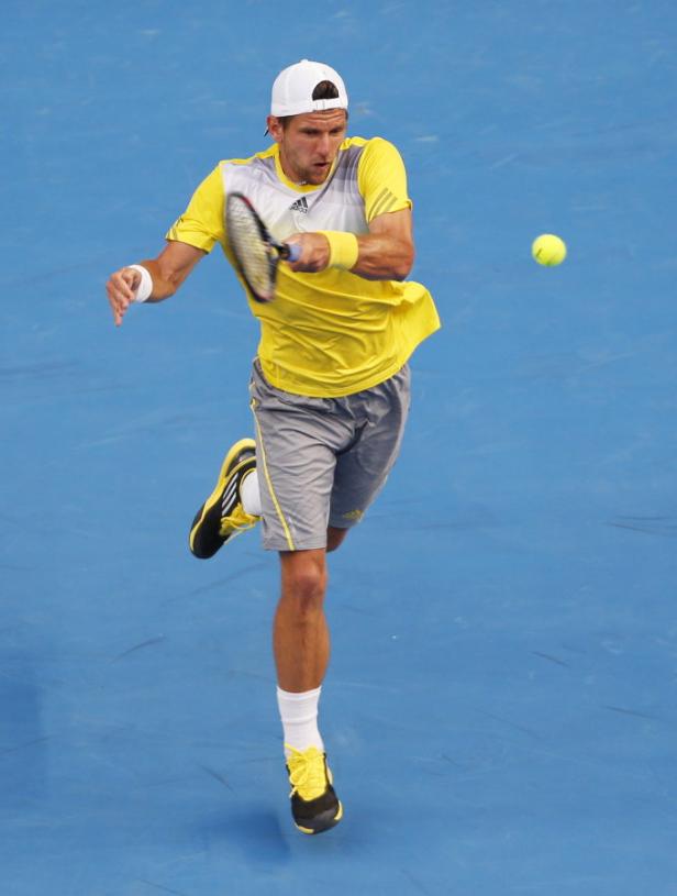 Ein Tennisspieler schlägt einen Ball auf einem blauen Platz.
