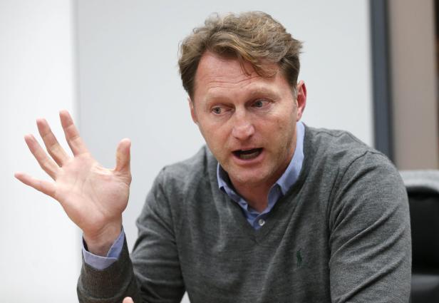 Ein Mann mit grauem Pullover gestikuliert während eines Gesprächs.