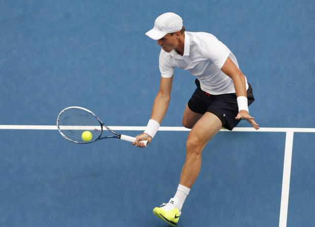 Ein Tennisspieler schlägt einen Ball auf einem blauen Platz.