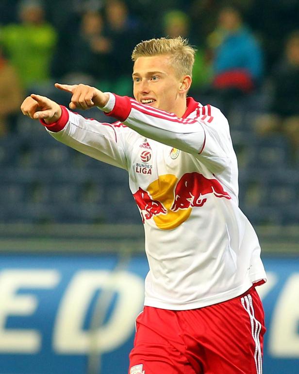 Ein Fußballspieler in rot-weißer Spielkleidung zeigt mit beiden Händen nach vorne.