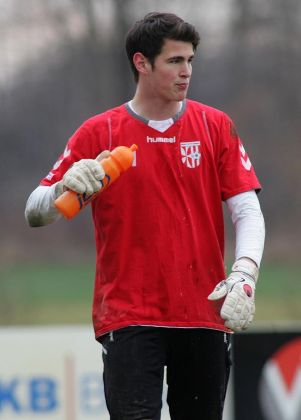 Ein junger Mann im Torwarttrikot hält eine orangefarbene Trinkflasche.