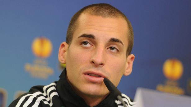 Ein Mann spricht in ein Mikrofon vor einem blauen Hintergrund.