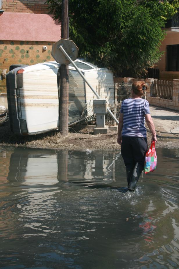 Eine Frau watet durch das Hochwasser an einem umgestürzten Wohnwagen vorbei.