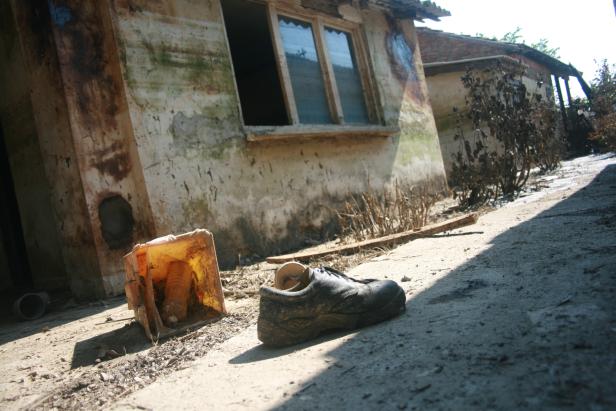 Ein schmutziger Schuh und eine Plastikkiste stehen vor einem verfallenen Haus.