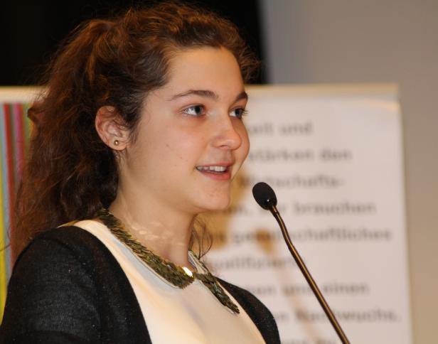 Eine junge Frau spricht bei einer Veranstaltung in ein Mikrofon.
