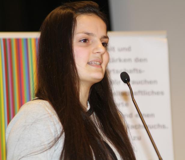 Eine junge Frau spricht bei einer Veranstaltung in ein Mikrofon.