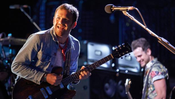 Ein Mann spielt auf einer Bühne Gitarre und singt in ein Mikrofon.