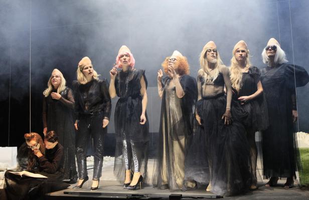 Eine Gruppe von Performer:innen in Kostümen und spitzen Hüten steht auf einer Bühne.