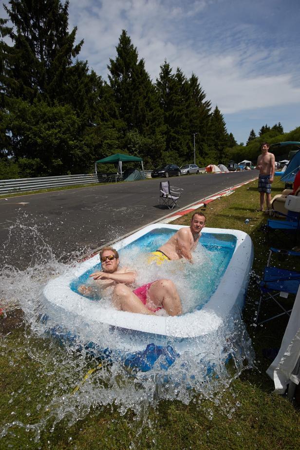 Zwei Männer planschen in einem aufblasbaren Pool neben einer Rennstrecke.