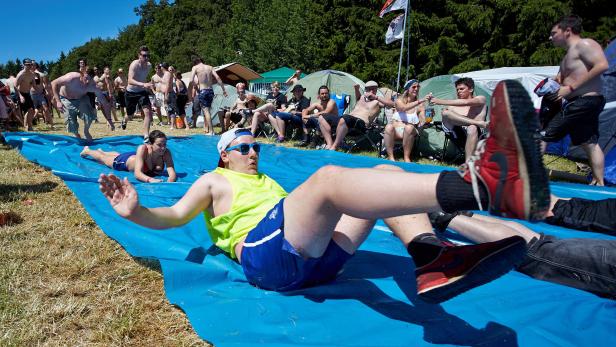 Menschen rutschen auf einer blauen Plane bei einem Sommerfest.