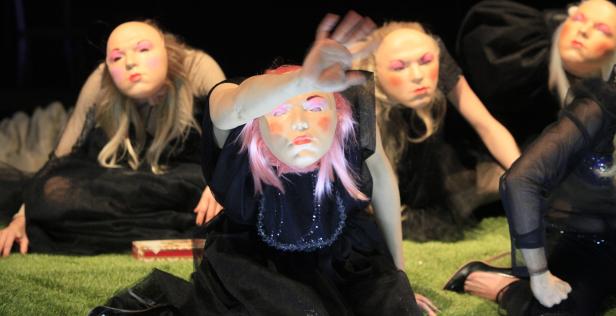 Eine Gruppe von Performerinnen mit Masken in einer Theaterszene.