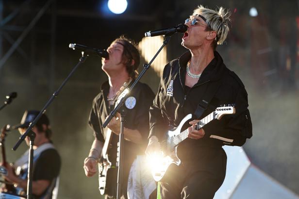 Zwei Musiker treten mit Gitarren und Mikrofonen auf einer Bühne auf.