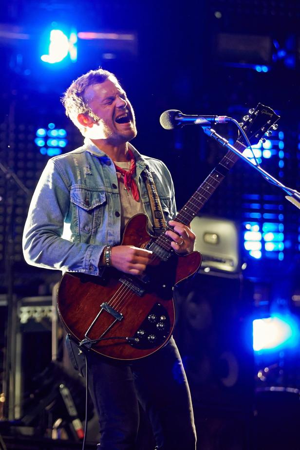 Ein Musiker spielt Gitarre und singt auf einer Bühne mit blauem Licht.