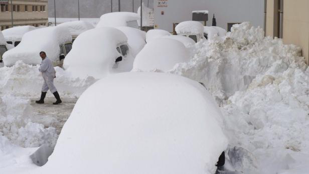 Ein Mann geht an einer Reihe von Autos vorbei, die mit Schnee bedeckt sind.