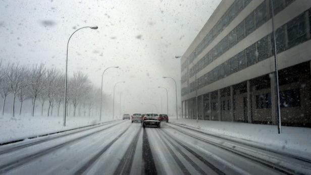 Autos fahren auf einer verschneiten Straße entlang eines Bürogebäudes.