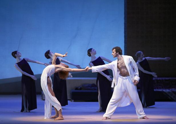 Eine Ballettaufführung mit einem Mann in Weiß und mehreren Tänzerinnen in dunklen Kleidern.