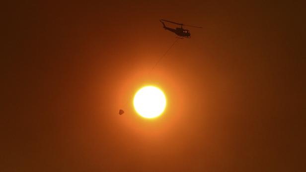 Ein Hubschrauber transportiert einen Wasserbehälter vor einer orangefarbenen Sonne.