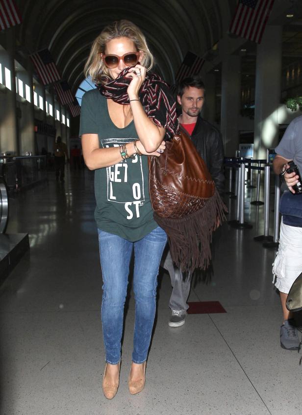 Eine Frau mit Schal und Sonnenbrille geht in einer Flughafenhalle entlang.