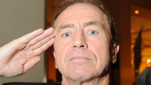Ein Mann mit blauen Augen grüßt mit der Hand an der Stirn.