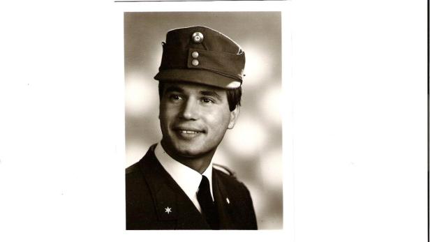 Ein junger Mann in Uniform und Mütze lächelt zur Seite.