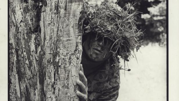 Ein Soldat mit Tarnkleidung versteckt sich hinter einem Baum.