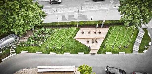 Ein Blick von oben auf einen begrünten Bereich mit Hochbeeten, einer Holzterrasse und einem Airstream-Wohnwagen.