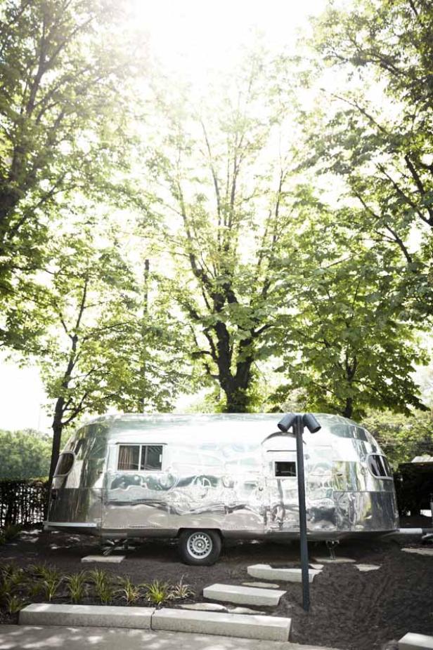 Ein silberner Airstream-Wohnwagen steht unter Bäumen.