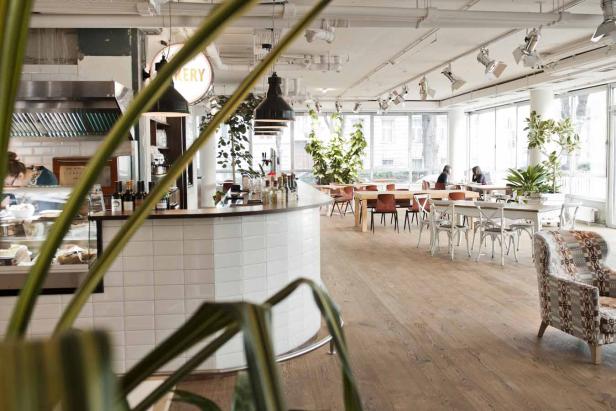 Innenansicht eines hellen Cafés mit Tischen, Stühlen und einer Theke.