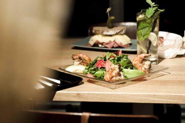 Ein Tisch mit einem Salat mit Garnelen, einem Sandwich und einem Getränk mit Minze.