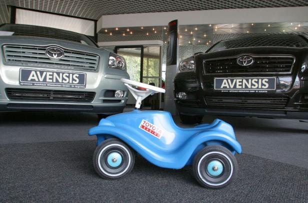 Ein blaues Kinderrutscherauto steht vor zwei Toyota Avensis in einem Autohaus.