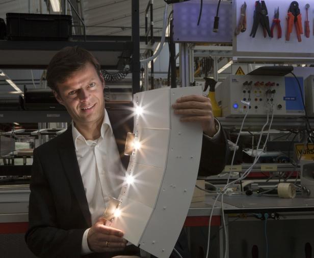 Ein Mann im Anzug hält ein LED-Paneel in einer Produktionsumgebung.